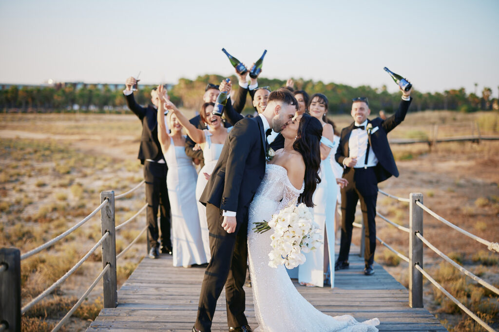 Brautpaar küsst sich mit Brautjungfern und Groomsmen auf einem Holzsteg im Vidamar Resort Algarve