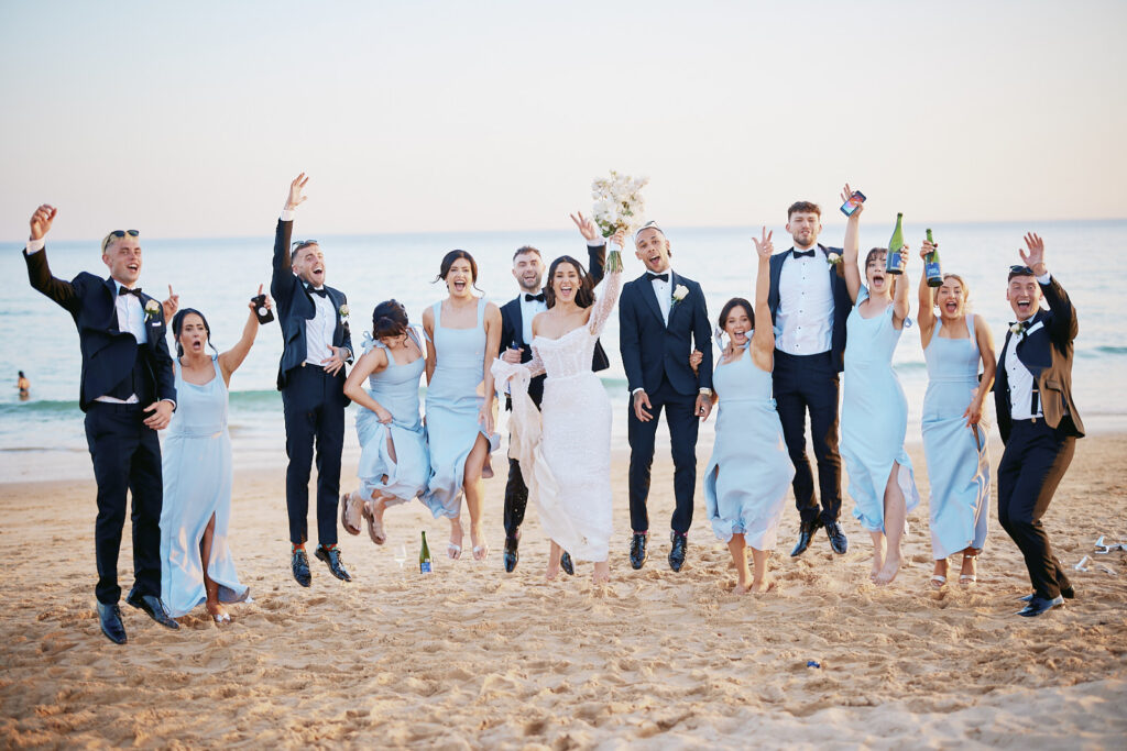 Brautpaar mit Brautjungfern und Groomsmen springt am Strand bei der Hochzeitsfeier im Vidamar Resort Algarve