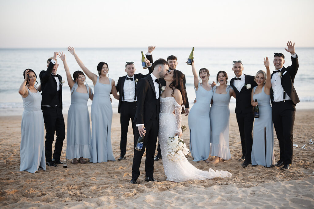 Brautpaar küsst sich mit Brautjungfern und Groomsmen am Strand im Vidamar Resort Algarve.