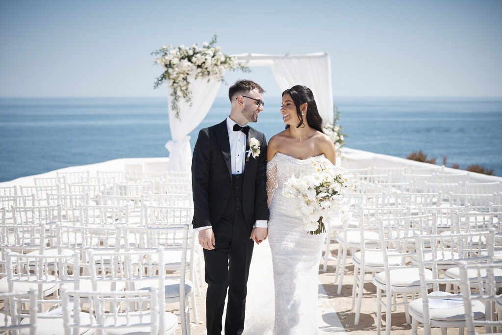 Brautpaar nach der Trauung in Senhora da Rocha an der Algarve zwischen den weißen Stuhlreihen am Meer