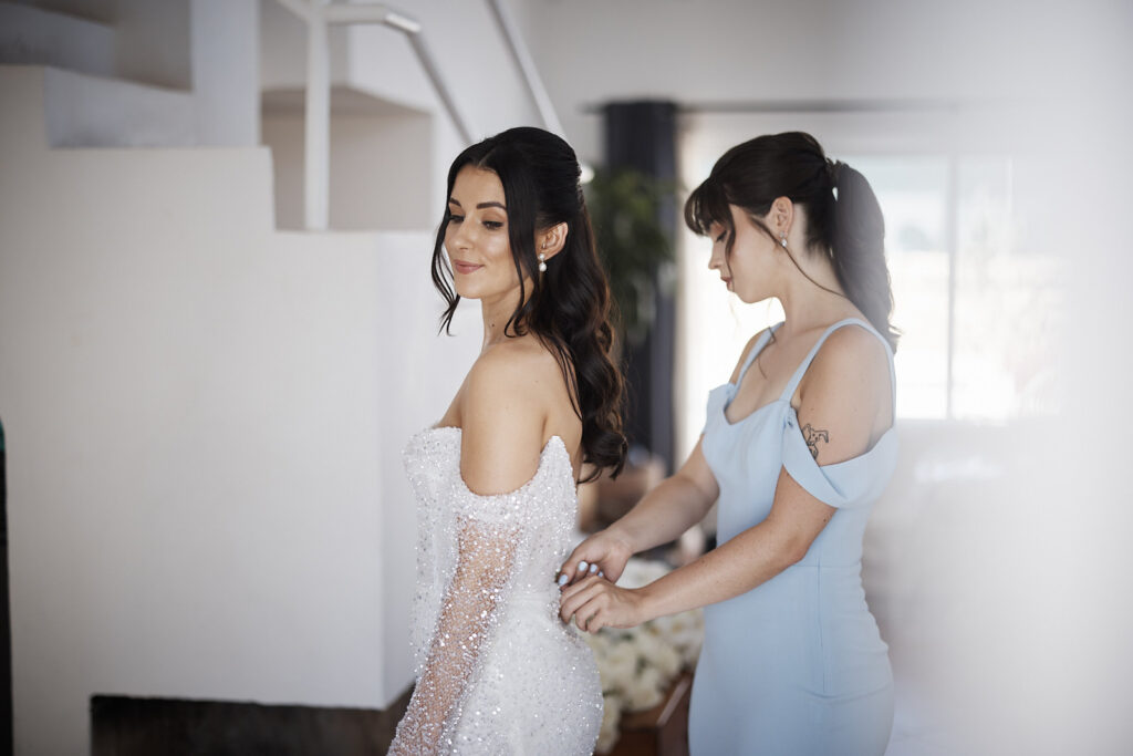 Brautjungfer hilft der Braut beim Schließen ihres Brautkleids während der Hochzeitsvorbereitung in Senhora da Rocha an der Algarve