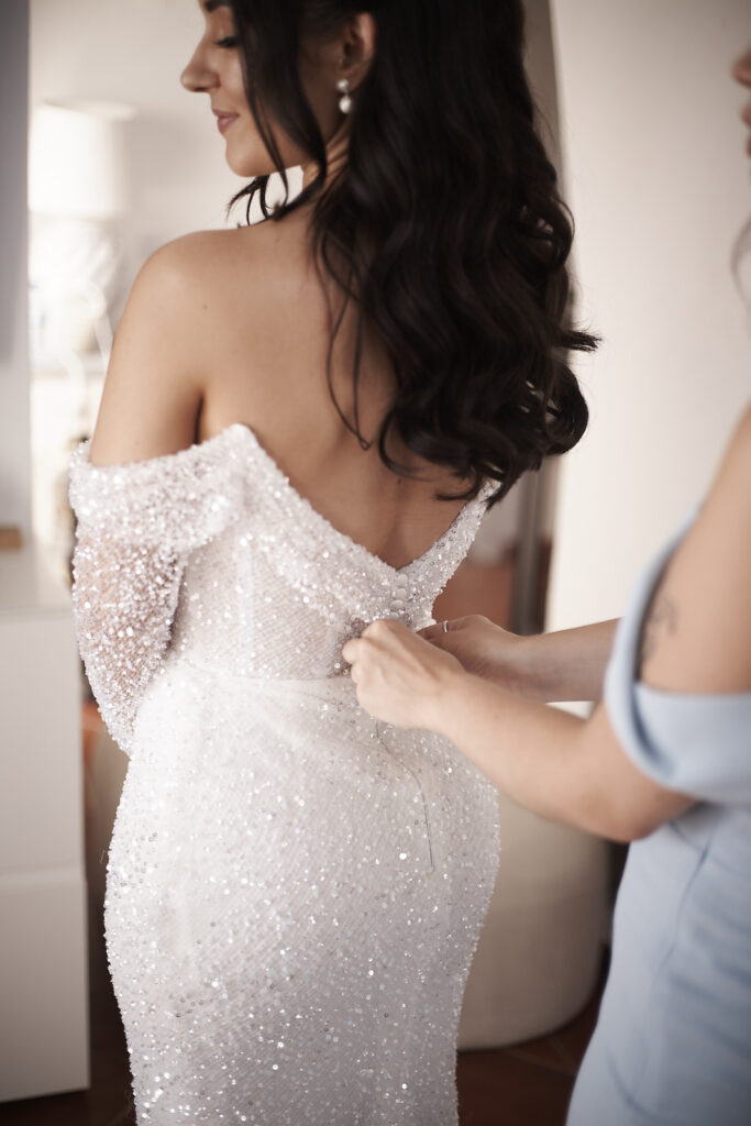 Braut wird während der Hochzeitsvorbereitung in Schwarzweiss in ihr Brautkleid geholfen in Senhora da Rocha an der Algarve