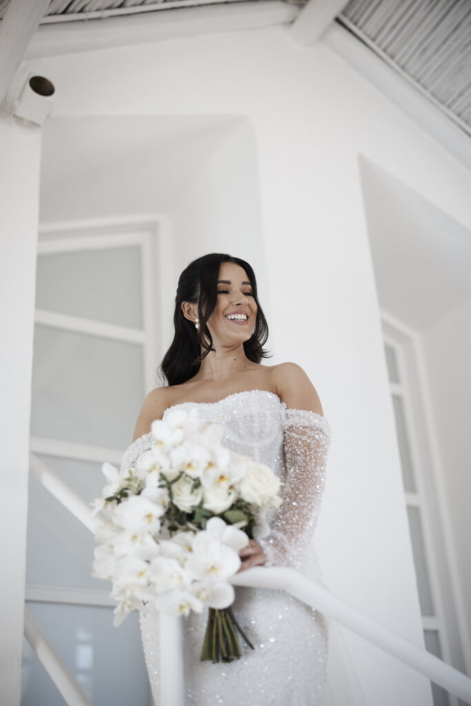 Braut auf einer Treppe mit weißem Brautstrauß während der Hochzeitsvorbereitung in Senhora da Rocha an der Algarve