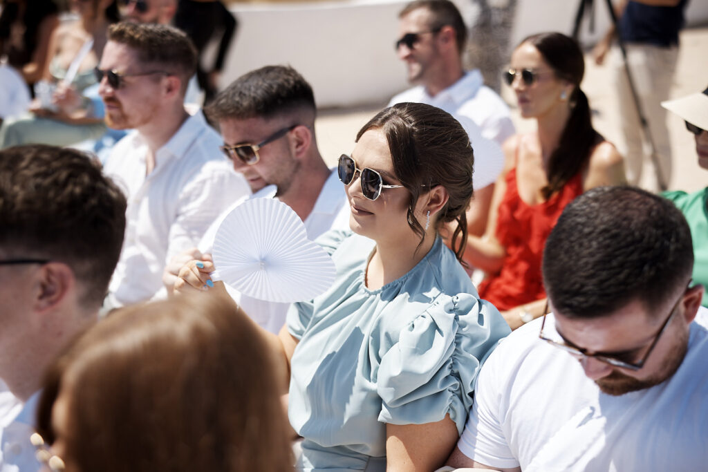 Hochzeitsgäste sitzen während der Trauung in Senhora da Rocha in der Sonne und fächeln sich Luft zu
