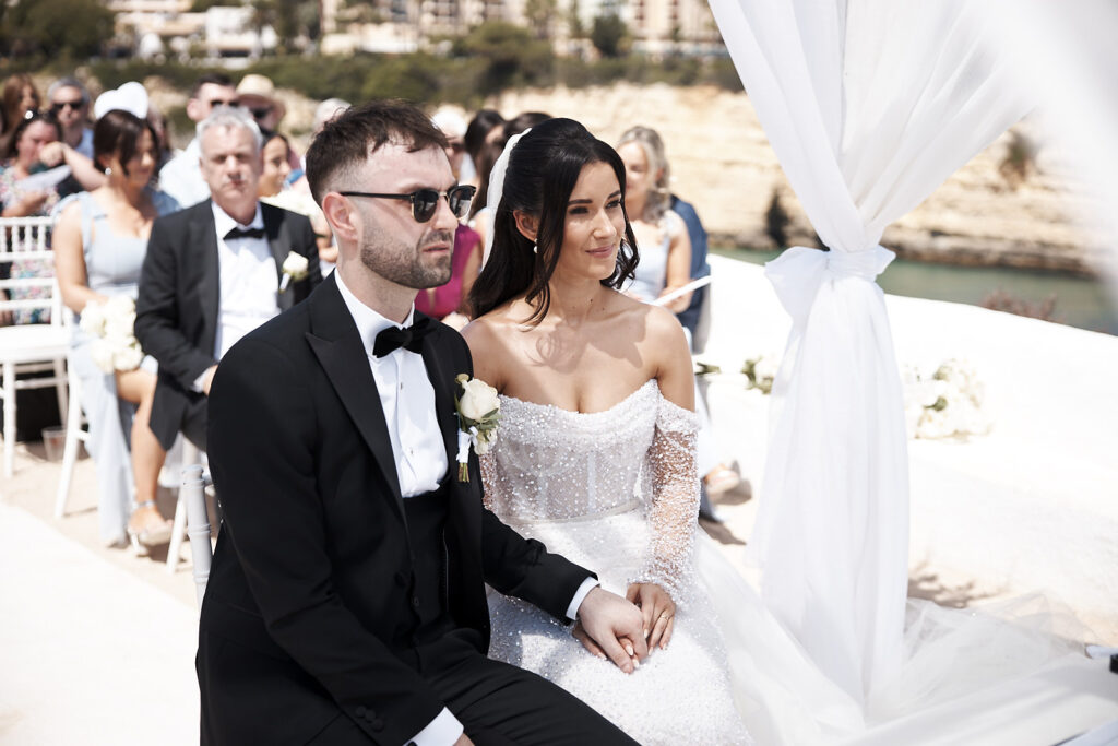 Braut und Bräutigam sitzen während der Trauung in Senhora da Rocha an der Algarve nebeneinander am Traubogen
