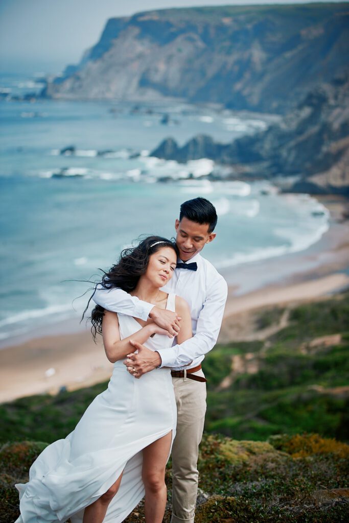 Bride and groom embracing on the cliffs above a beach during their Algarve elopement in Portugal.
