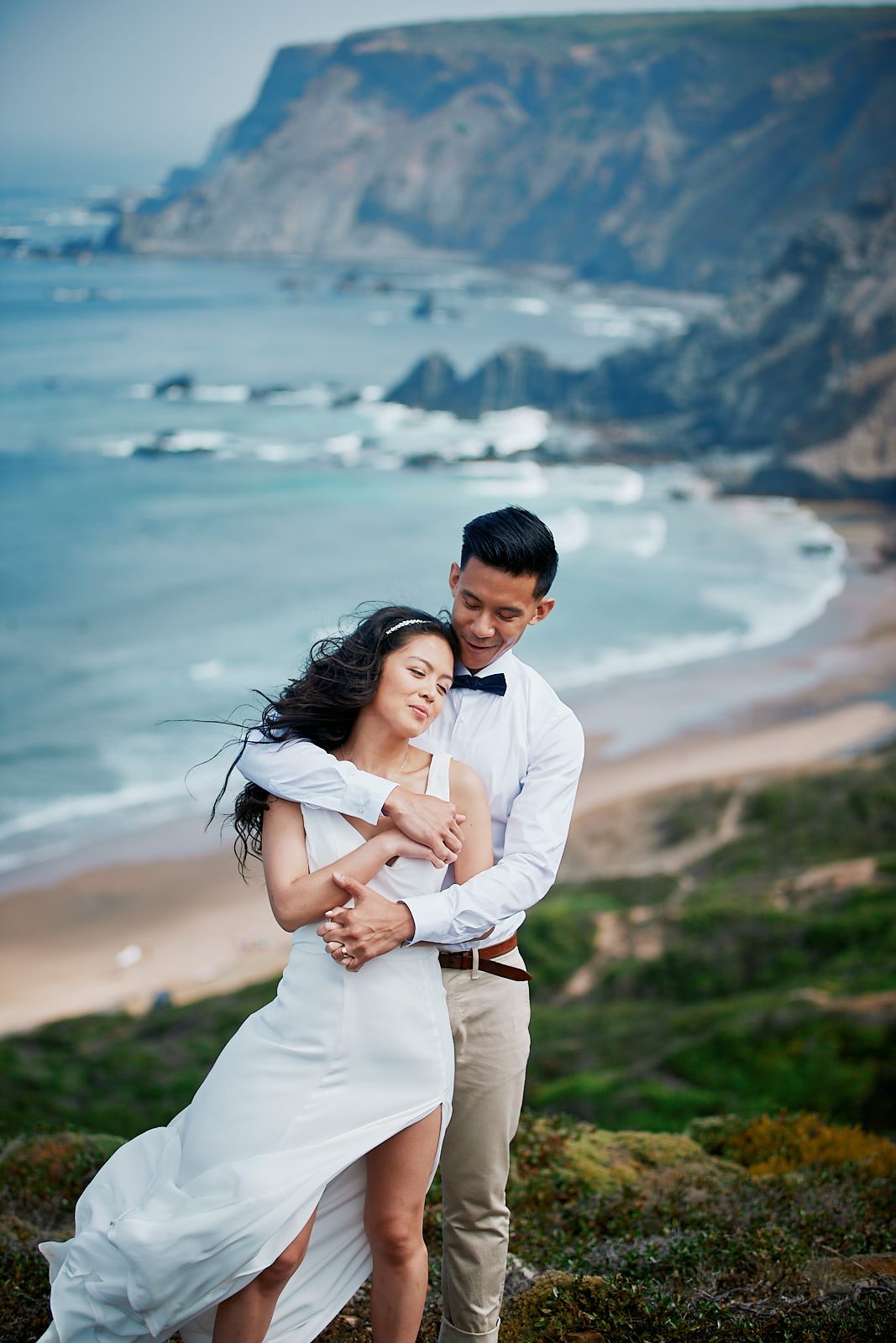 Bride and groom embracing on the cliffs above a beach during their Algarve elopement in Portugal.
