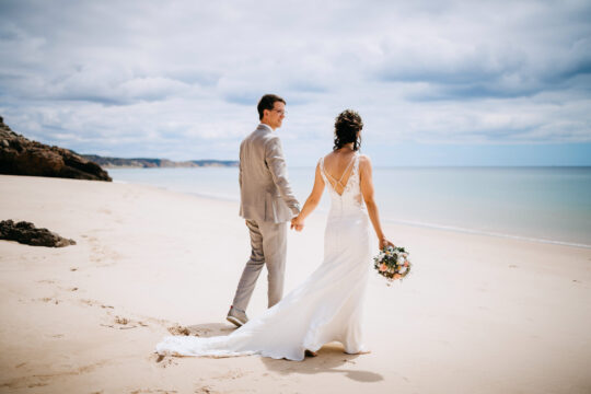 Brautpaar geht Hand in Hand am Strand der Algarve nach einer Hochzeit zu zweit in Portugal