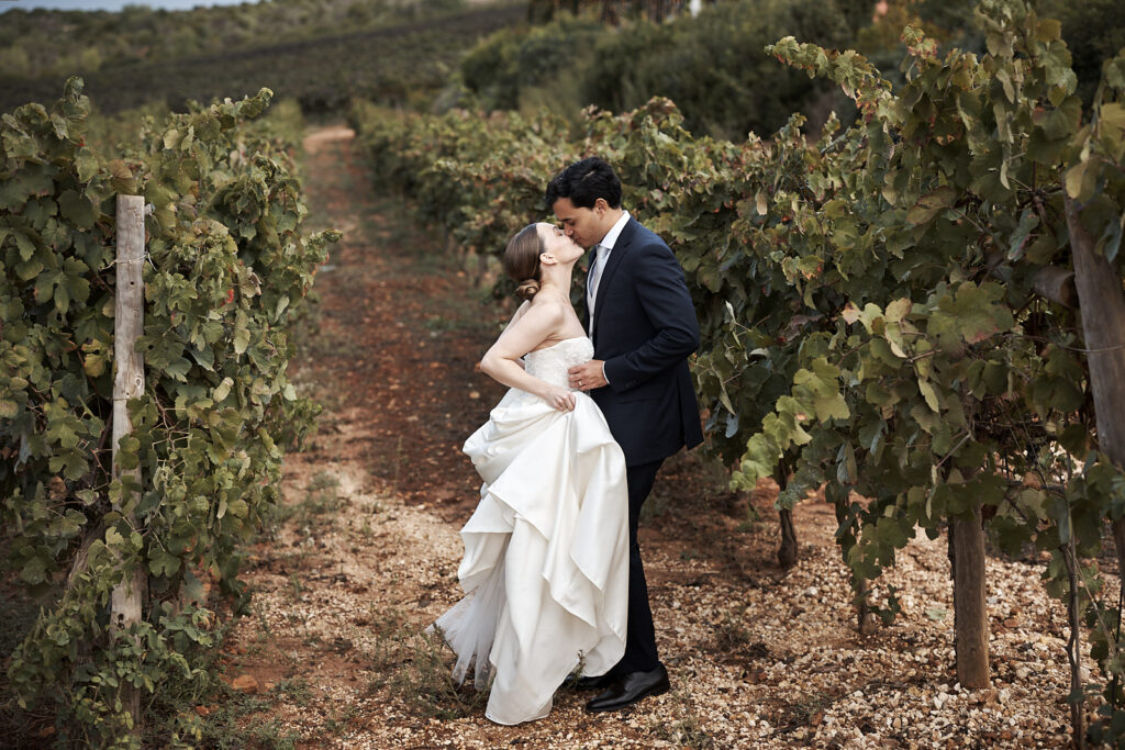 Braut und Bräutigam küssen sich zwischen den Weinreben auf dem Weingut Arvad in der Algarve