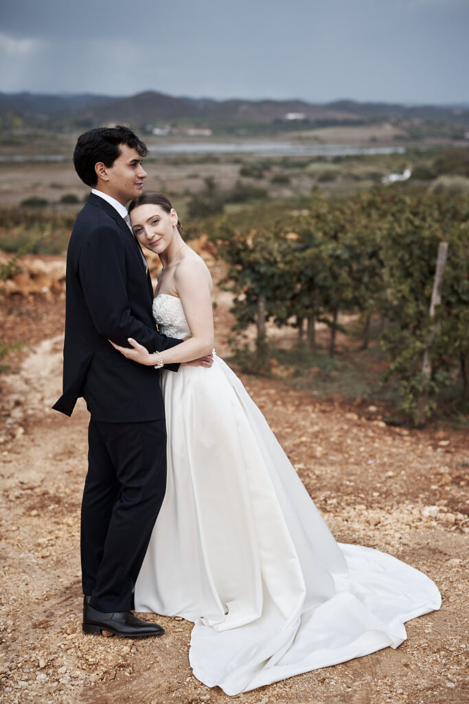 Braut und Bräutigam stehen eng umarmt vor den Weinbergen auf dem Weingut Arvad in der Algarve