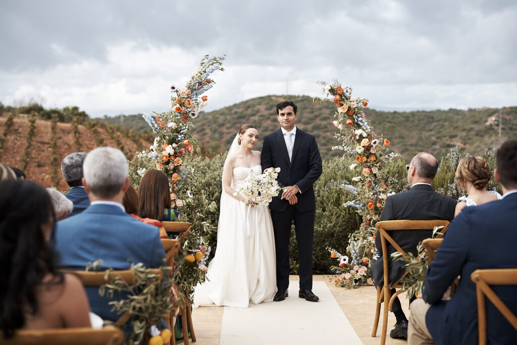 Brautpaar unter floralem Traubogen während der freien Trauung auf dem Weingut Arvad in der Algarve