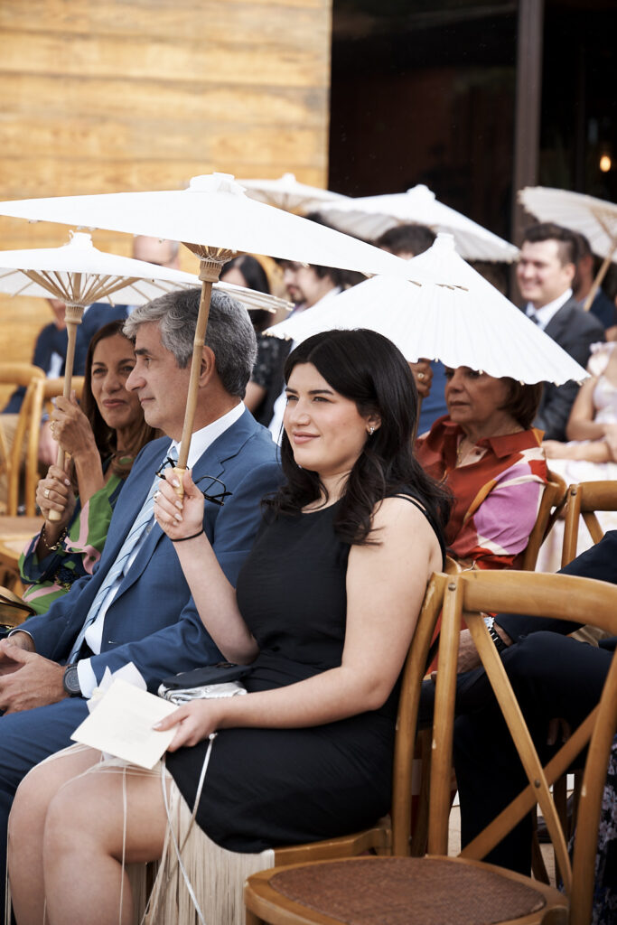 Hochzeitsgäste sitzen mit weißen Sonnenschirmen während der freien Trauung auf dem Weingut Arvad in der Algarve
