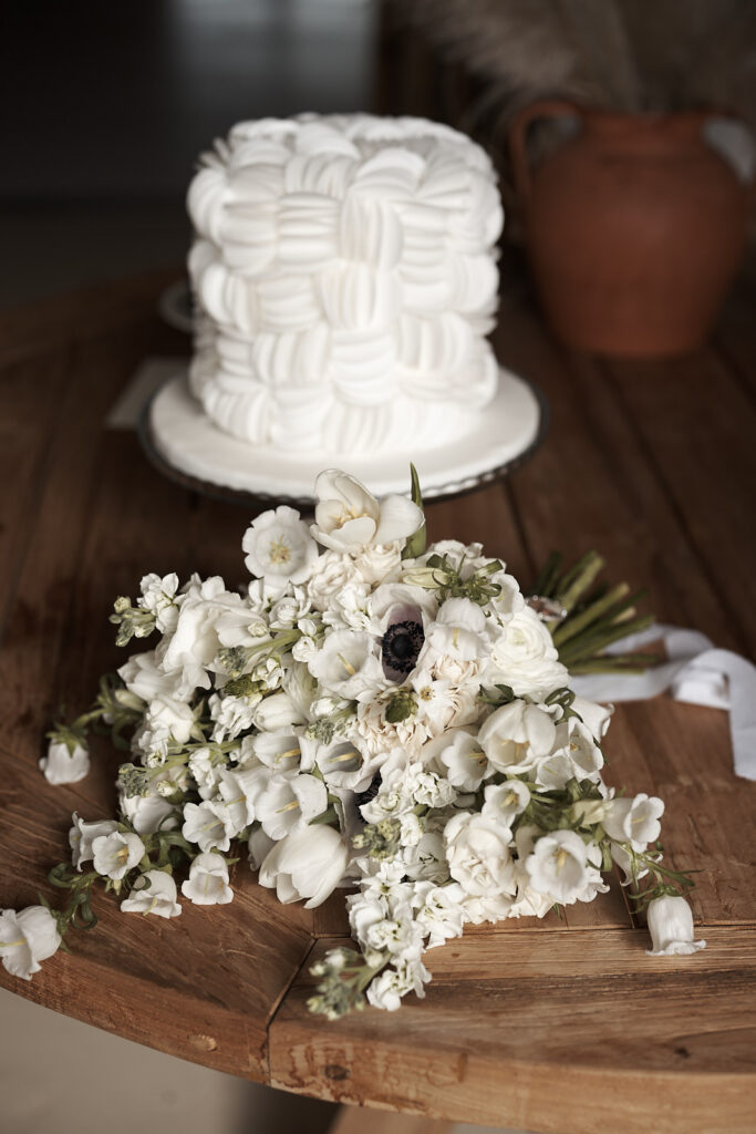 Brautstrauß mit weißen Blumen vor einer modernen Hochzeitstorte auf einem Holztisch auf dem Weingut Arvad in der Algarve