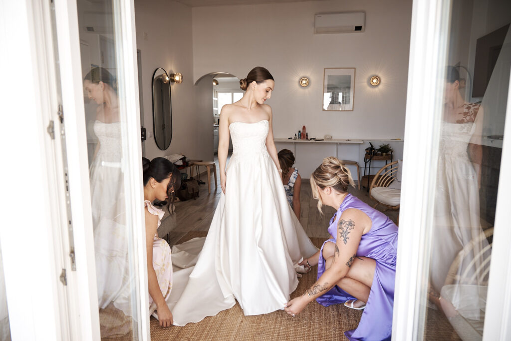 Braut beim Ankleiden mit ihren Freundinnen in einer hellen Suite vor der Hochzeit im Weingut Arvad an der Algarve