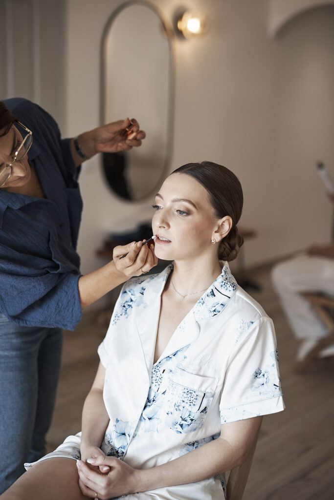 Braut im floralen Pyjama beim Lippen-Make-up während der Vorbereitungen zur Hochzeit im Weingut Arvad