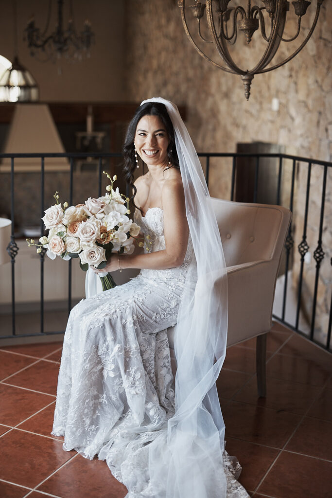 Braut mit Schleier sitzt mit Brautstrauß während der Hochzeitsvorbereitungen im Monte do Serrinho an der Algarve, Portugal