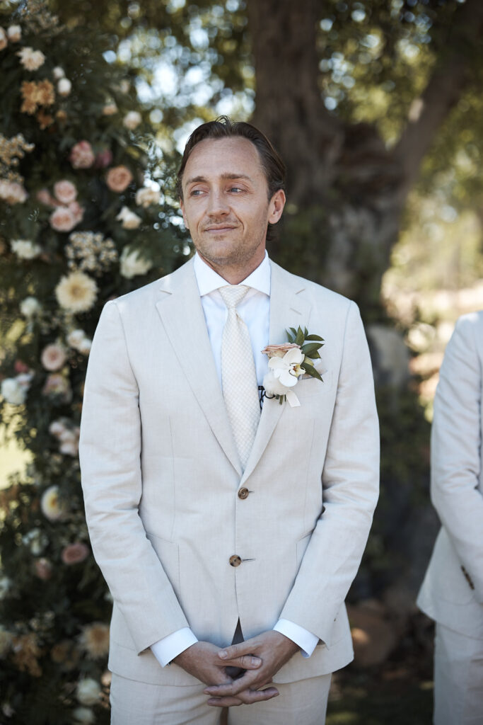 Natürliches Brautporträt während der Hochzeitsvorbereitungen im Monte do Serrinho an der Algarve, Portugal. Die Braut sitzt mit langem Schleier und einem eleganten Brautstrauß aus Rosen und Orchideen im Innenbereich der Hochzeitslocation.