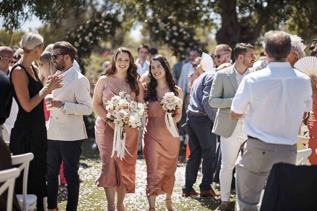 Zwei Brautjungfern mit Blumensträußen gehen nach der Trauung durch die Gäste im Monte do Serrinho an der Algarve