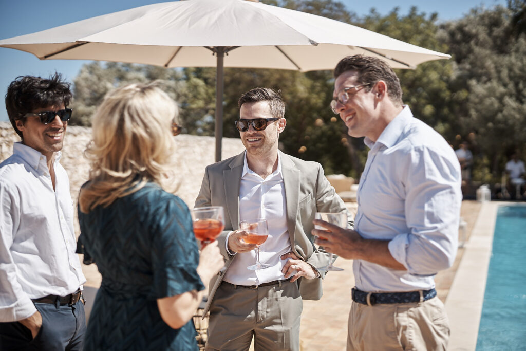 Hochzeitsgäste stehen mit Drinks am Pool der Hochzeitslocation Monte do Serrinho an der Algarve