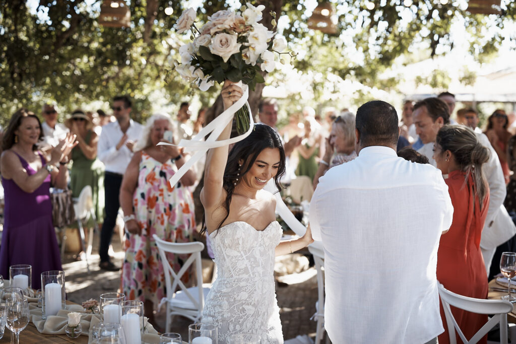 Braut hebt ihren Brautstrauß beim Empfang zwischen applaudiernden Hochzeitsgästen im Monte do Serrinho an der Algarve