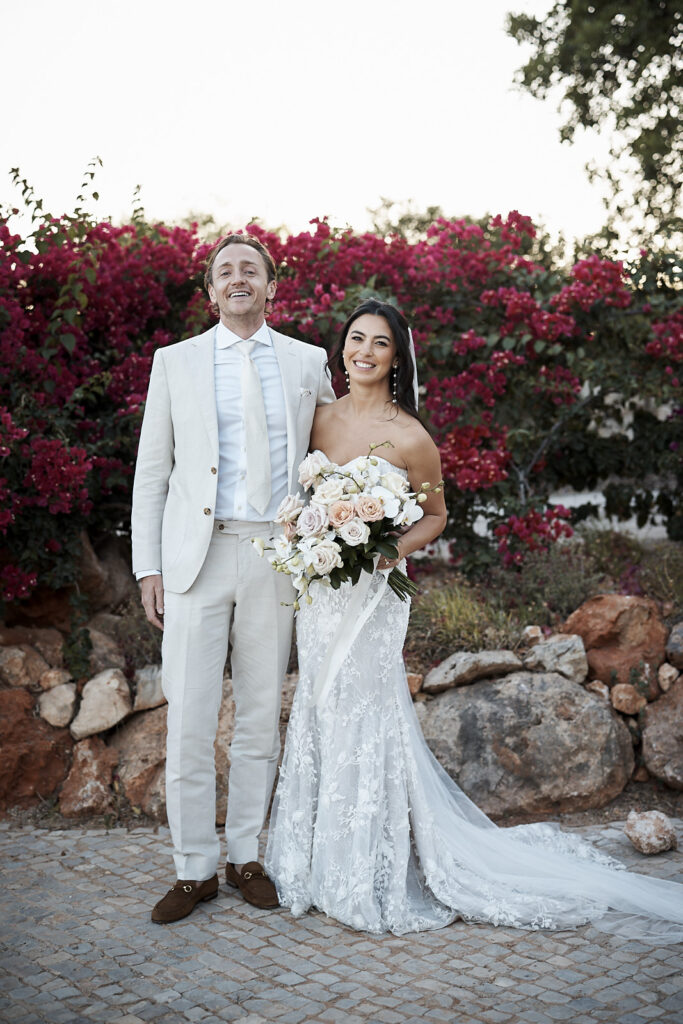 Braut und Bräutigam posieren mit Brautstrauß vor pinken Bougainvillea im Monte do Serrinho an der Algarve