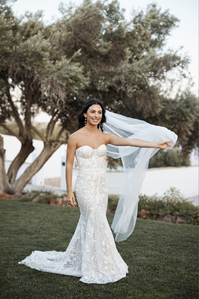 Braut steht im Garten von Monte do Serrinho an der Algarve und hält ihren Schleier im Abendlicht