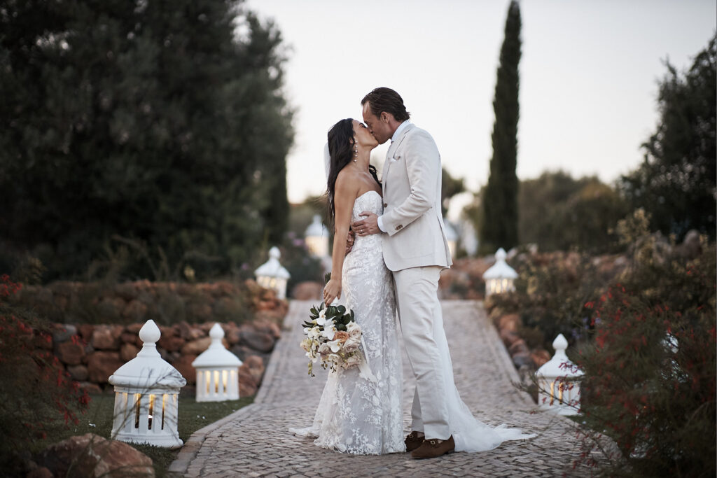 Braut und Bräutigam küssen sich auf einem Gartenweg im Monte do Serrinho an der Algarve