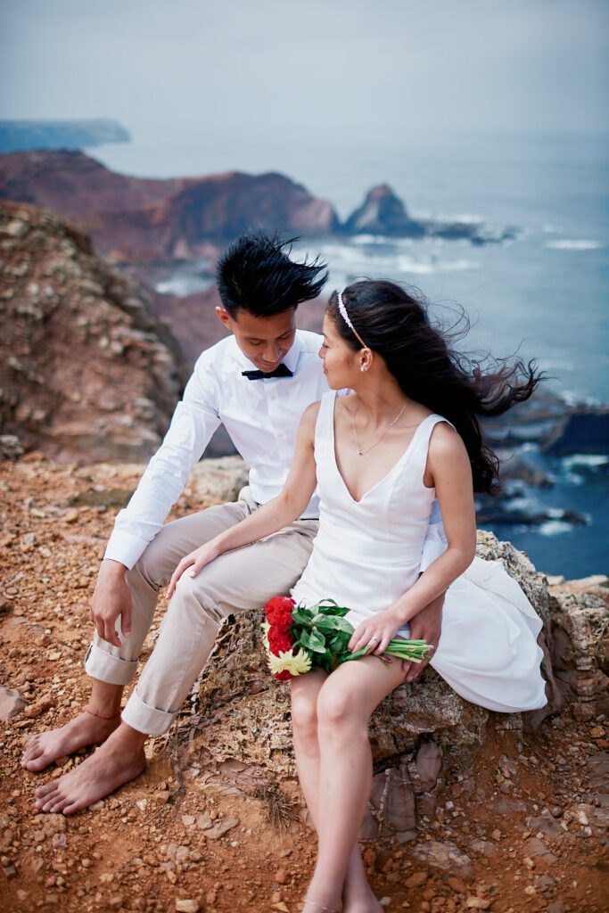 Couple sitting on the cliffs overlooking the Atlantic during an intimate Algarve elopement in Portugal.
