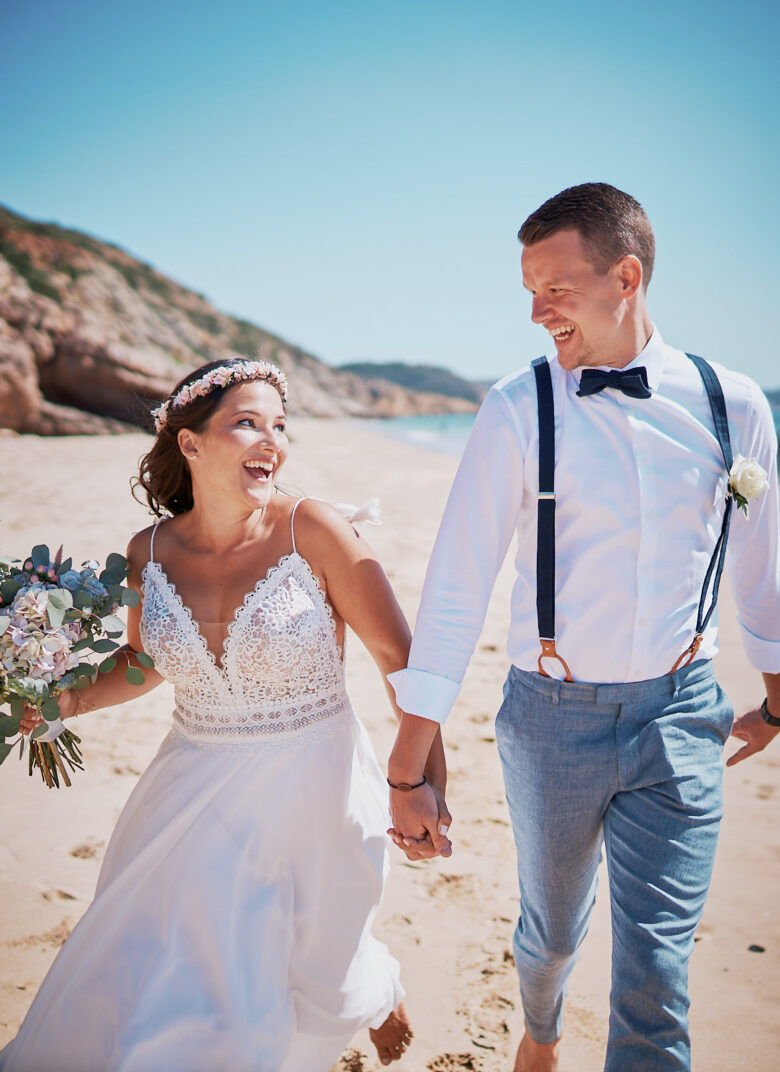 Brautpaar läuft nach einer Strandhochzeit an der Algarve barfuß am Strand entlang
